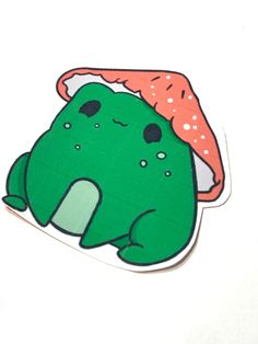 a green sticker with a red hat on it's head sitting next to a white wall