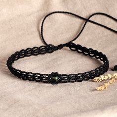 a close up of a black string bracelet with an earring on top of it