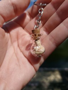 a hand holding a tiny glass bottle with sand in it and a key chain attached to it