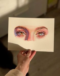 a person holding up a piece of paper with an image of their eyes painted on it