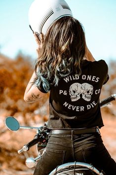 a woman riding on the back of a motorcycle wearing a t - shirt that says wild ones never die