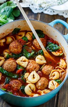 a pot filled with meatballs and spinach in tomato sauce next to a wooden spoon