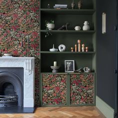 a living room with green bookshelves and floral wallpaper on the walls next to a fireplace