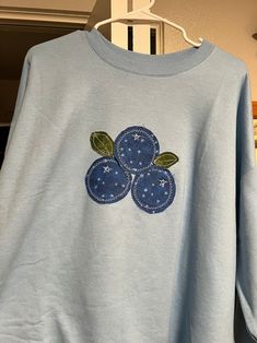 a blue sweatshirt with three flowers embroidered on the front and two green leaves on the back