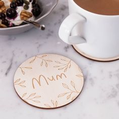 a cup of coffee sitting next to a bowl of cereal and a plate with the word mum on it