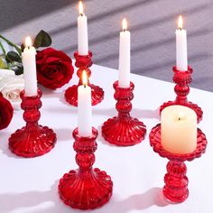 red glass candlesticks on a white table with roses