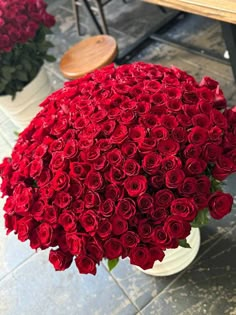 a large bouquet of red roses sitting on top of a white vase next to a wooden bench