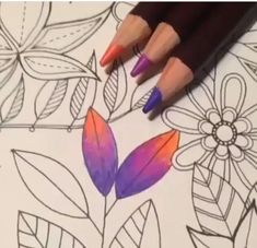 some colored pencils are laying on top of a coloring book with flowers and leaves