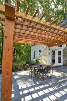 an outdoor patio with table and chairs under a pergolated arbor in front of a house