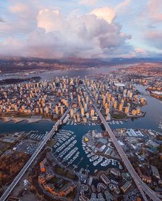 an aerial view of a large city with lots of boats in the water and clouds