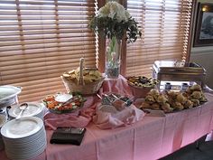 a table covered in plates and food next to a window with blind shades on it