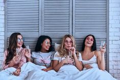 three women laying in bed drinking champagne and smiling at the camera with their eyes closed