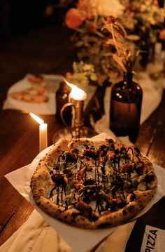 a pizza sitting on top of a wooden table next to candles and flowers in vases