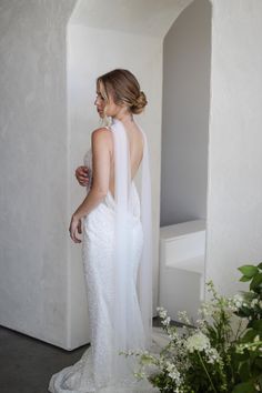 a woman standing in front of a mirror wearing a white dress and holding a bouquet