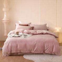 a bed with pink sheets and pillows on top of it next to a white lamp