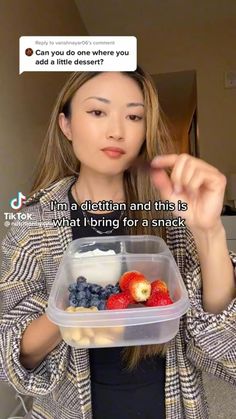 a woman is holding a plastic container with fruit in it and pointing to the side