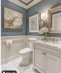 a white toilet sitting next to a bathroom sink under a framed flower painting on the wall