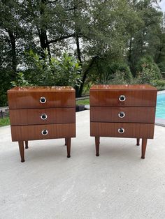 two wooden dressers sitting next to each other on top of a cement floor in front of a swimming pool