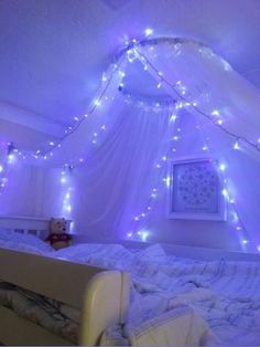 a bed with white sheets and purple lights on the ceiling