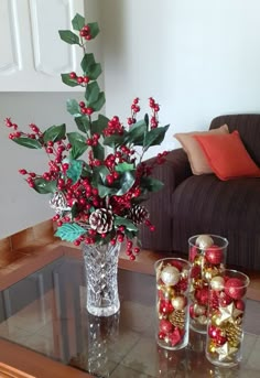 a vase filled with red berries and pine cones on top of a glass coffee table