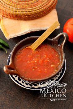 a bowl of tomato sauce with a wooden spoon in it on a plate next to tomatoes