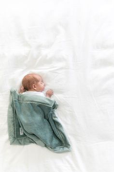 a baby wrapped in a blanket laying on top of a white bedding covered in blankets