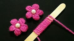 two pink crocheted flowers on top of a wooden skewer next to a knitting needle