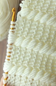 a close up view of a white crochet blanket with yellow pins on it