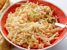 a red bowl filled with coleslaw next to a baguette and napkin