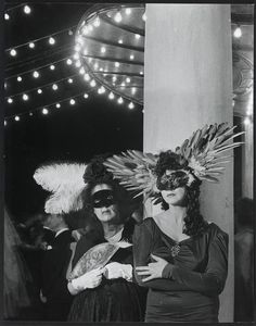 black and white photograph of two women dressed in costumes with feathers on their head standing next to each other