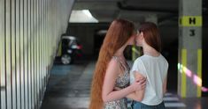 two young women standing next to each other in a parking garage, one with long red hair