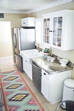 a kitchen with white cabinets and an area rug in front of the sink, refrigerator and dishwasher