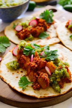 three tortillas with meat and veggies are on a wooden platter