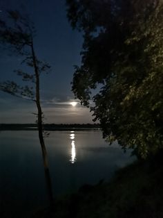 the full moon is shining in the night sky over water with trees on either side