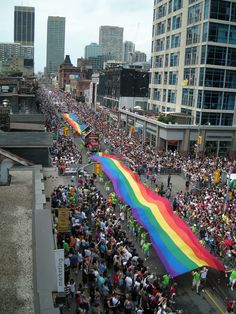 a large rainbow flag is being carried down the street