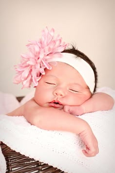 a baby is sleeping on top of a wicker basket with a pink flower in it's hair