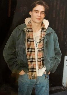 a young man standing in front of a door wearing a plaid scarf and green jacket