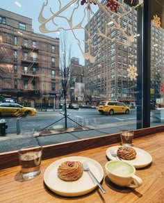 two plates with food sit on a table in front of a window overlooking a city street