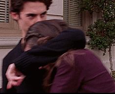 a man and woman are hugging in front of a house