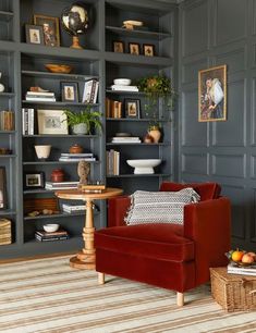 a living room filled with lots of bookshelves next to a red chair and table