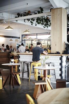 people sitting at tables in a restaurant with plants hanging from the ceiling and on the walls