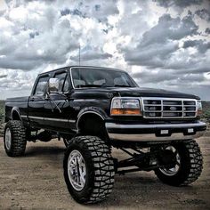 a black truck parked on top of a dirt field under a cloudy sky with clouds in the background