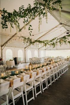 an indoor tent with tables and chairs set up for a formal dinner or function, surrounded by greenery