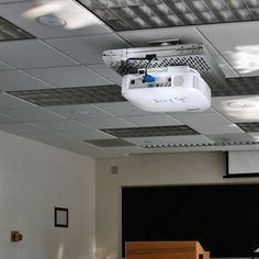 an empty classroom with desks and chairs in front of a projector screen on the ceiling