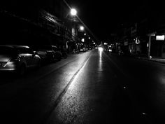 cars are parked on the side of an empty street at night in black and white