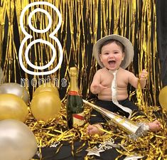 a baby is sitting in front of gold foil balloons and champagne bottles with the number eight on it