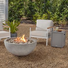 an outdoor fire pit with chairs and a table in front of it on gravel ground