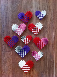 six hearts made out of perler beads on a wooden surface with white and red dots