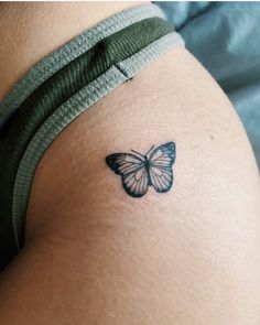 a small butterfly tattoo on the back of a woman's thigh, it is black and white