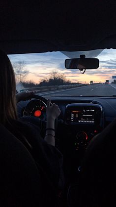 two people driving in the dark on a highway at sunset or dawn with their hands on the steering wheel